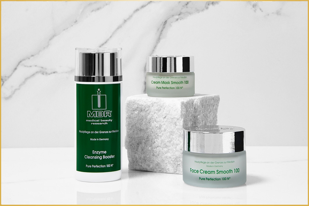 MBR skincare products including Enzyme Cleansing Booster, Cream Mask Smooth 100, and Face Cream Smooth 100 on a marble surface.
